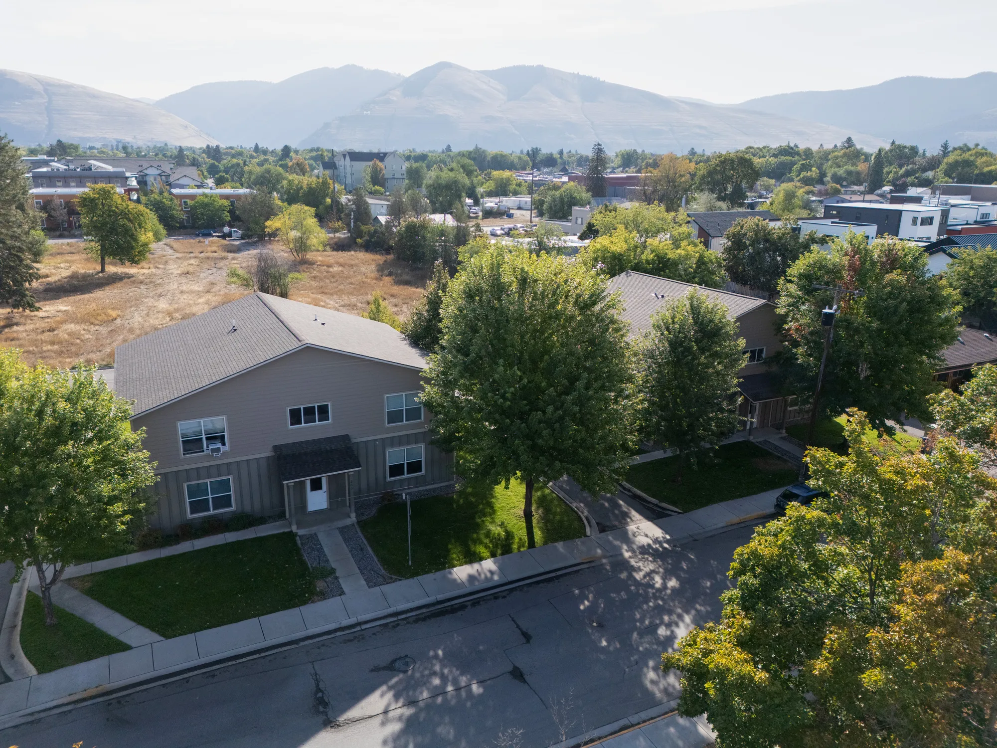 Aerial view of an apartment building surrounded by trees, with mountains in the distance